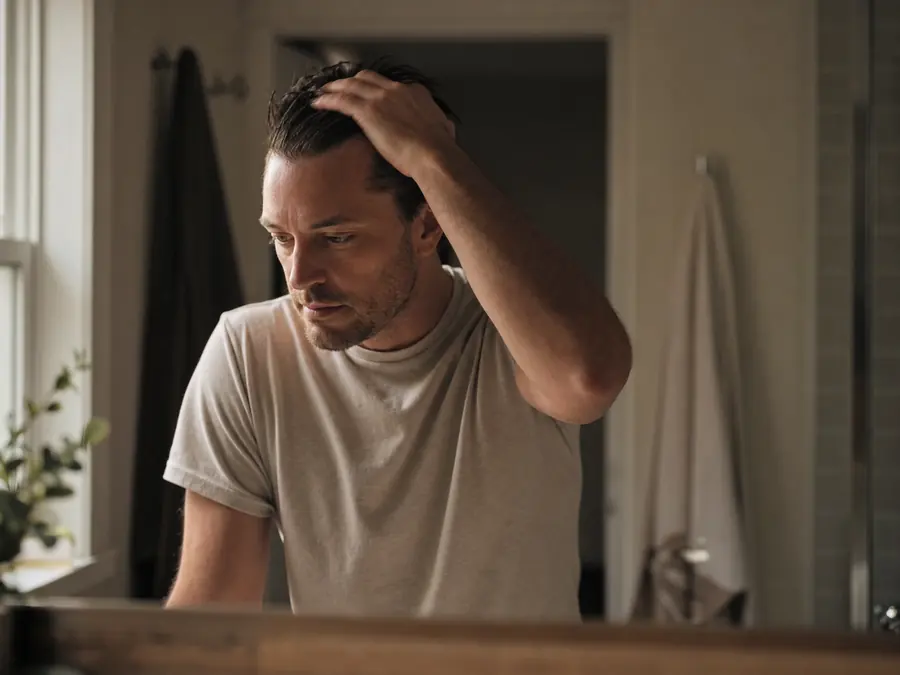 A man looking in the bathroom mirror, pushing his hair back